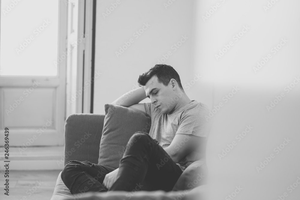Fototapeta premium Young attractive man suffering from depression in emotional pain lying on couch at home