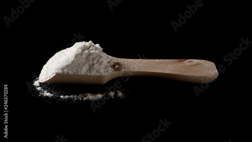 Wheat flour pile in wooden spoon isolated on black background, powder texture