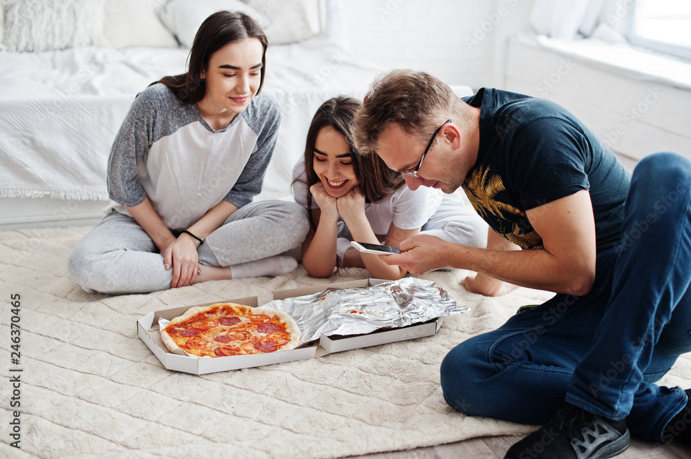 Friends enjoying and spending time together. Twins girls with pizza box. Man looking on mobile phone.