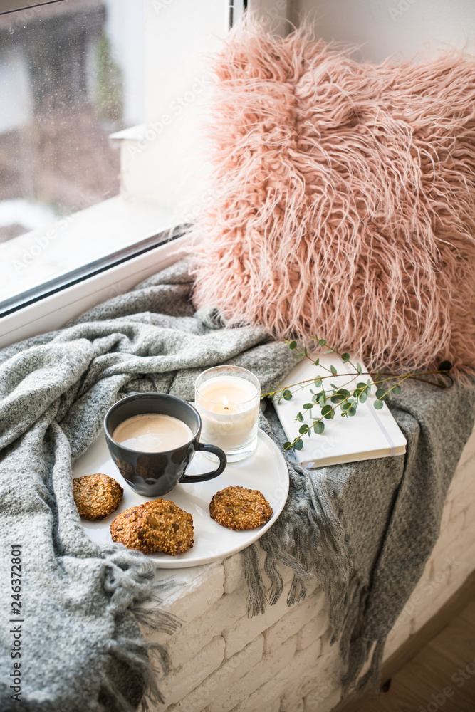 Fototapeta premium Scandinavian style breakfast, cup of coffee and cookies on cozy windowsill with warm blanket and pillow
