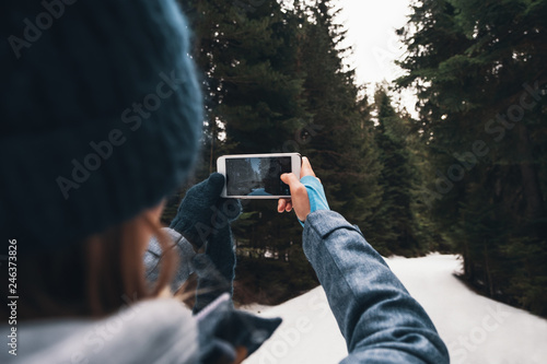 Back view woman taking picture of winter forest by smartphone