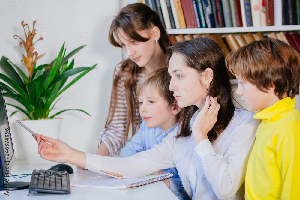 Group of elementary pupils in computer class with female teacher. Four different age pupils working together. Teaching children to do common project concept.