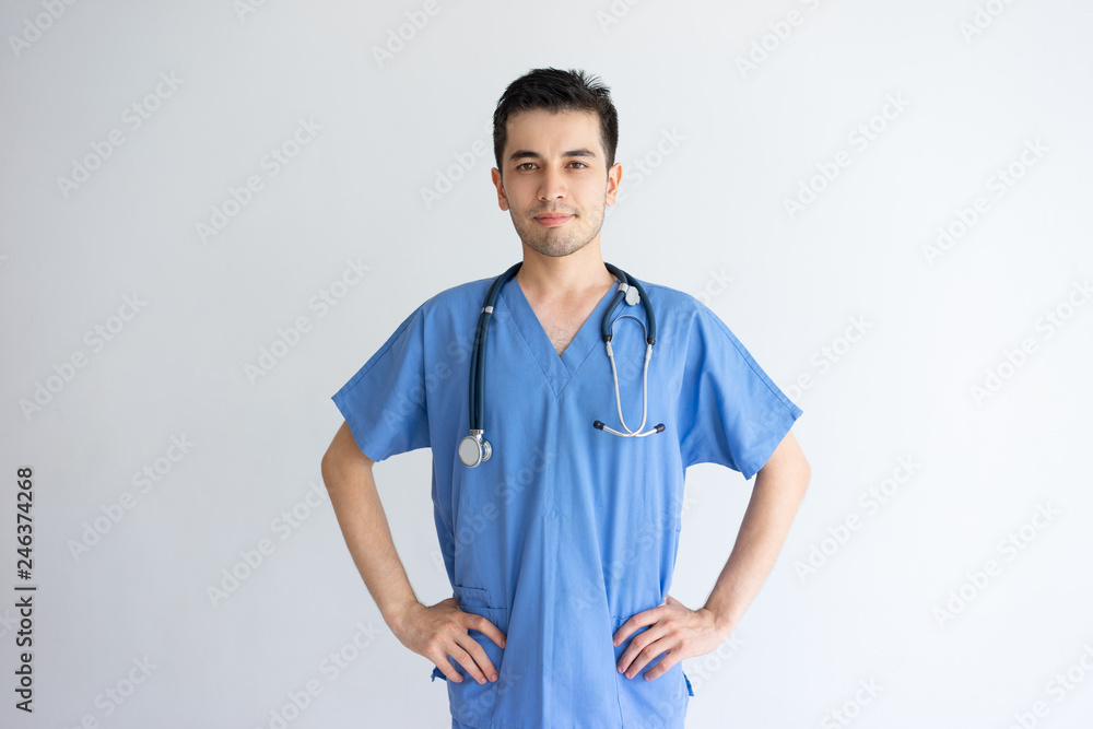 Content handsome young male physician posing at camera. Handsome guy standing and wearing blue medical uniform. Medicine concept. Isolated front view on white background. Content handsome young male physician posing at camera. Handsome guy standing and wearing blue medical uniform. Medicine concept. Isolated front view on white background.