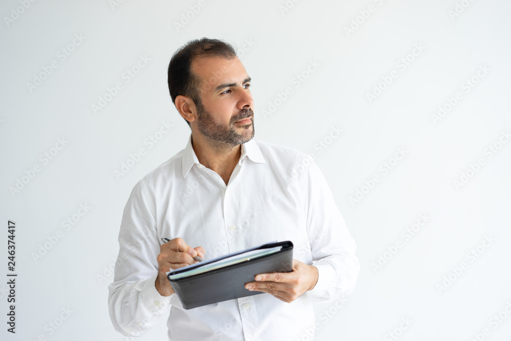 Pensive handsome man holding file and writing. Business man thinking and working. Paperwork concept. Isolated front view on white background. Pensive handsome man holding file and writing. Business man thinking and working. Paperwork concept. Isolated front view on white background.