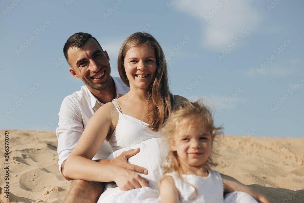 Happy family with daughter in white clothes are sitting toghether in desert sand dune. Happy family with daughter in white clothes are sitting toghether in desert sand dune.