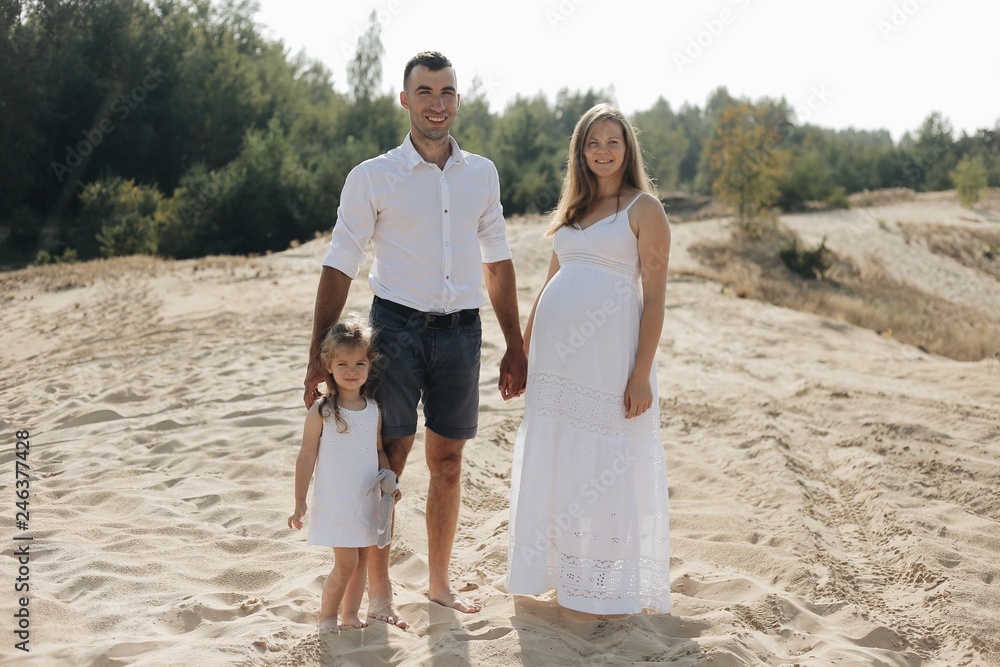 Portrait of caucasian family with baby in white clothes are standing on sands dune. Pregnant mpther. Newborn Portrait of caucasian family with baby in white clothes are standing on sands dune. Pregnant mpther. Newborn