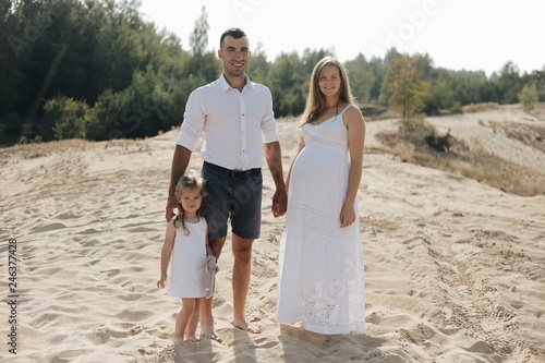Portrait of caucasian family with baby in white clothes are standing on sands dune. Pregnant mpther. Newborn © sqofield135178