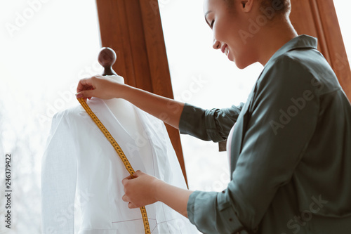 Young designer with tape is measuring white shirt. Side view photo