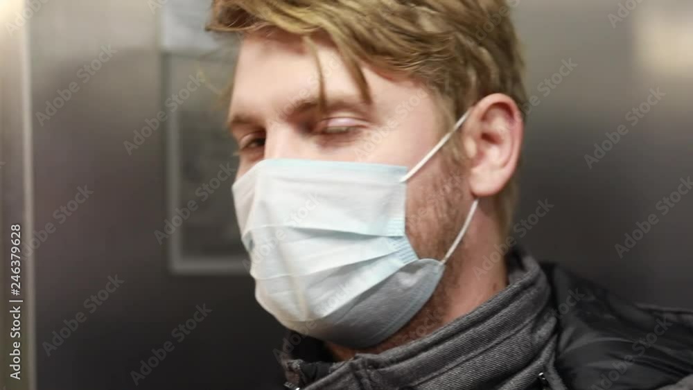Young guy wearing antiviral face mask for flu influenza in elevator sickness infection pandemic virus pandemy, respiratory health vaccine Young guy wearing antiviral face mask for flu influenza in elevator sickness infection pandemic virus pandemy, respiratory health vaccine