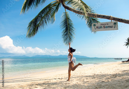 The girl in a white dress jumps to the palm trees on the beach of Samui Island