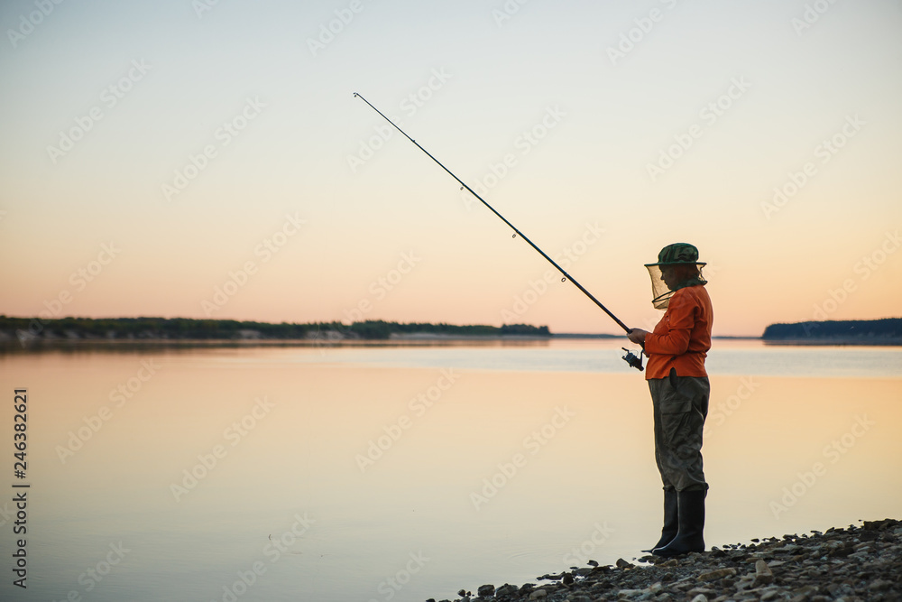 Young woman in mosquito net fishing with fishing rod in the evening.