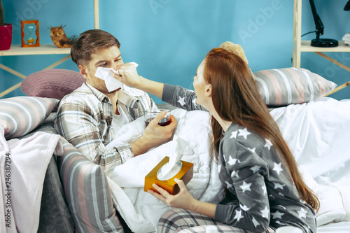 Sick man with fever lying in bed having temperature. The his wife take care for him. The illness, influenza, pain, family concept. Relaxation at Home. Healthcare Concepts.
