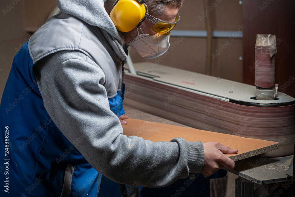 man in safety glasses, headphones and a respirator work for a grinding machine