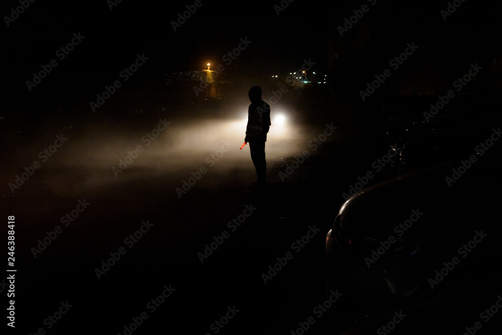 Silhouette of unrecognizable man illuminated by the headlights of a car on a dark night.