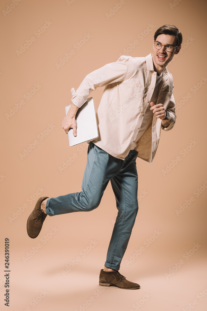 happy man in glasses running with laptop on beige background happy man in glasses running with laptop on beige background