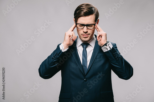 confident businessman in glasses touching temples isolated on grey