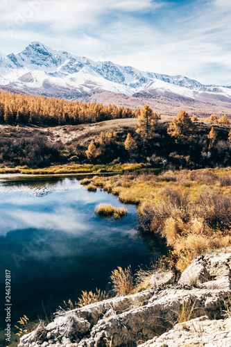 Reflection of mountains and clouds in clear surface of lake. Golden autumn in mountains.