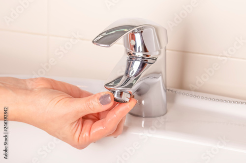 The girl's hand twists off twists the faucet aerator in the bathroom.
