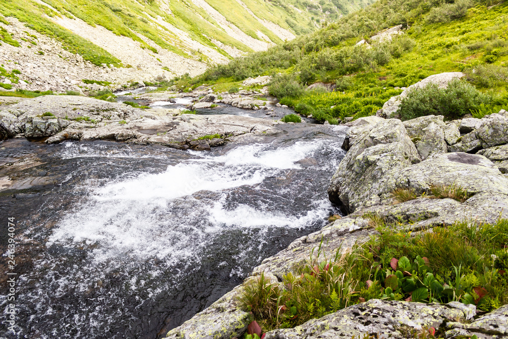 Spring waterfall in mountain valley. Fast river with green shores Spring waterfall in mountain valley. Fast river with green shores
