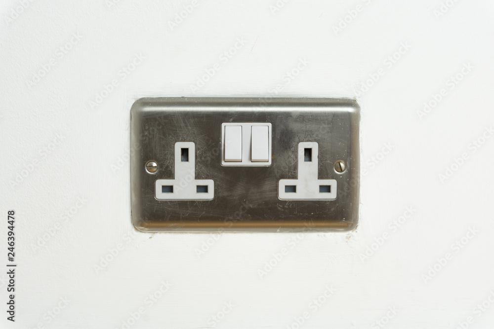 Stainless steel UK plug socket on white wall Stainless steel UK plug socket on white wall