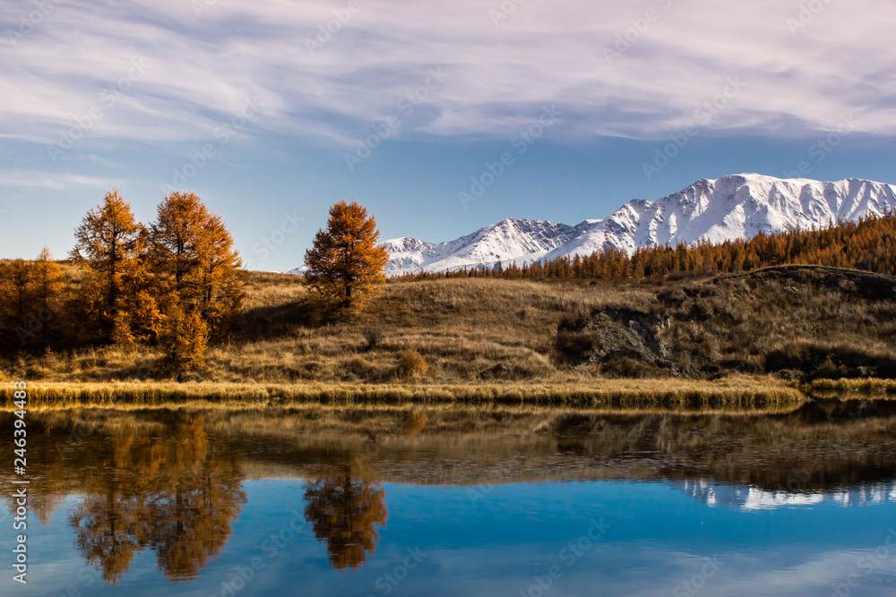 Reflection of mountains and clouds in clear surface of lake. Golden autumn in mountains.