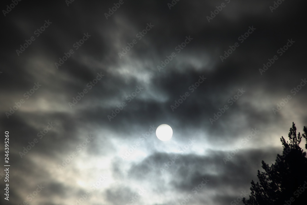 Dramatic white winter full moon behind the black clouds