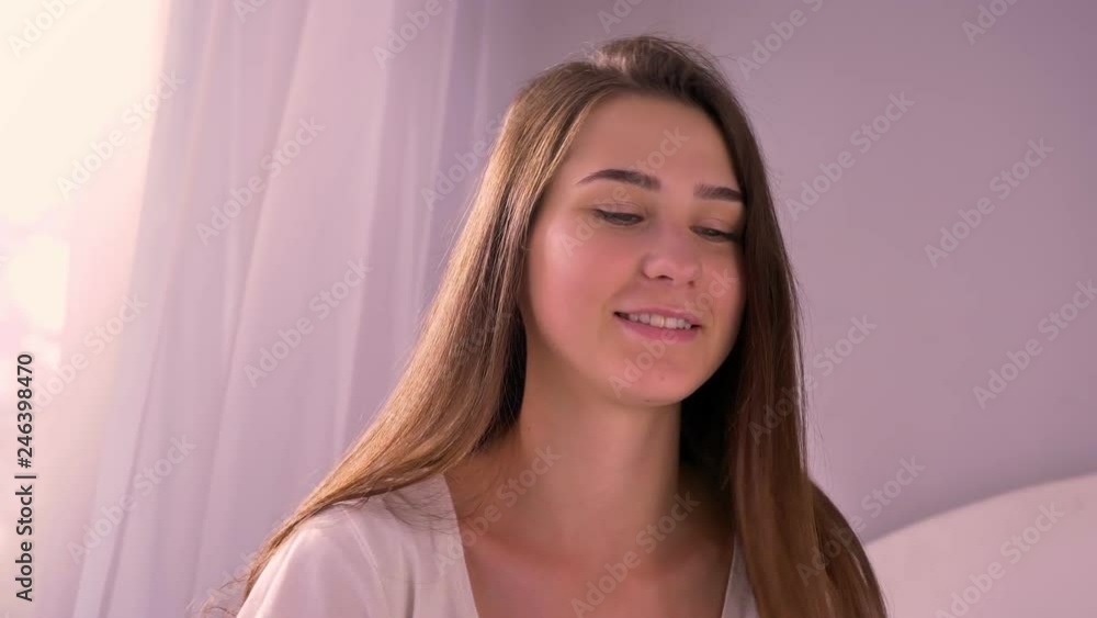 Closeup portrait of young beautiful caucasian female smiling singing while listening to music and looking at camera in the bedroom indoors Closeup portrait of young beautiful caucasian female smiling singing while listening to music and looking at camera in the bedroom indoors