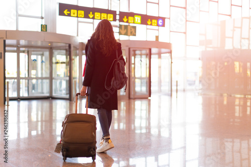 Rear view of brunette woman exit from airport with trolley (hand luggage)