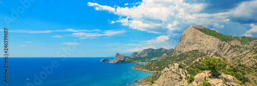 Scenic view of rocky mountains overgrown green trees and clear azure water of sea at sunny day on background beautiful blue sky. Beautiful sea landscape, panoramic banner 