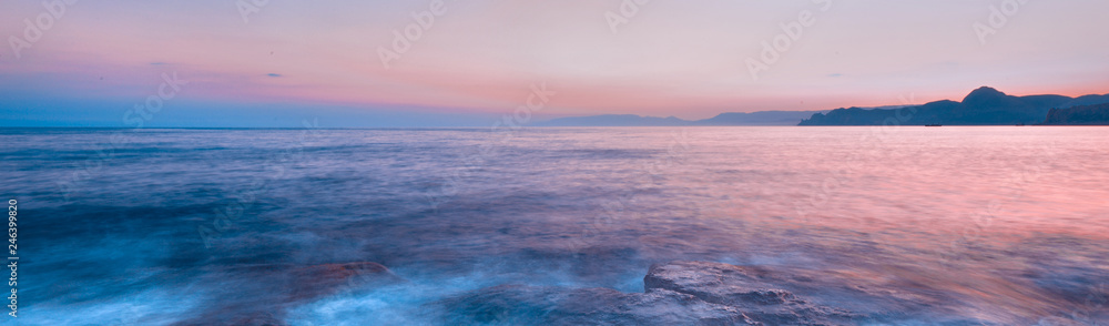 Beautiful mysterious marine landscape at sunset. Mountains, volcanic reef and ocean, panoramic banner.