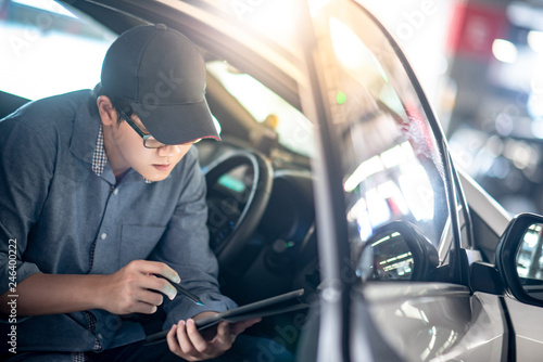 Asian auto mechanic sitting on driver seat checking the car using digital tablet in auto service garage. Mechanical maintenance engineer working in automotive industry. Automobile servicing and repair © zephyr_p