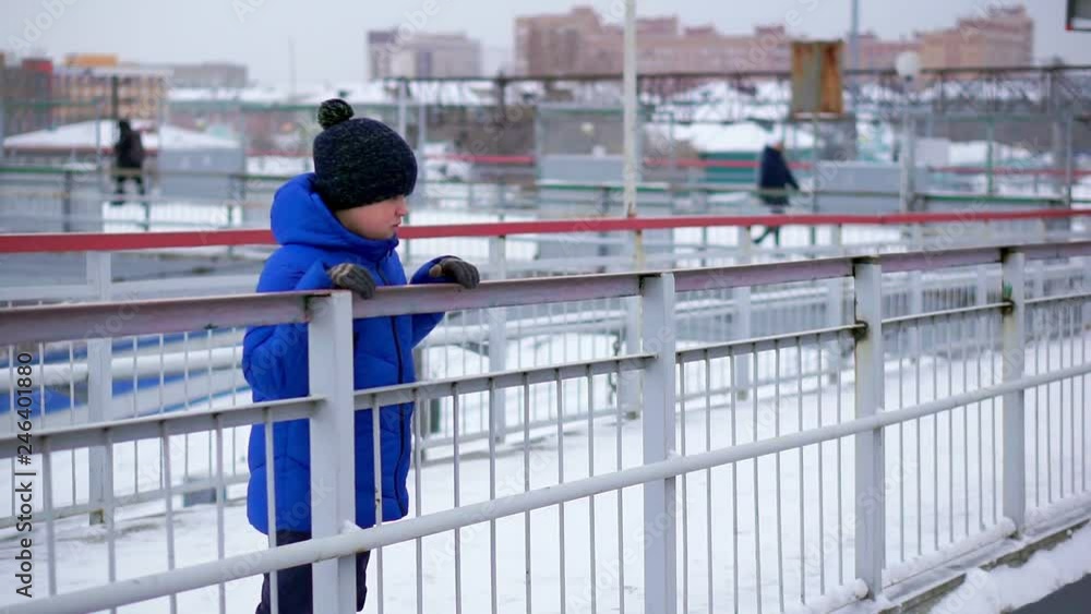 Boy teenager in blue down jacket lost in the city. He is at the train station, looking down. Boy teenager in blue down jacket lost in the city. He is at the train station, looking down.
