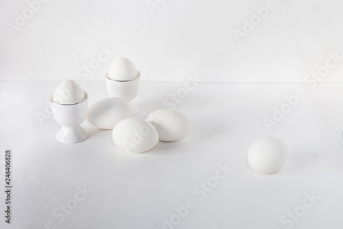 minimalistic composition of two white eggs in a stand and four white eggs lying on a white background. Perfect breakfast. copy place for text