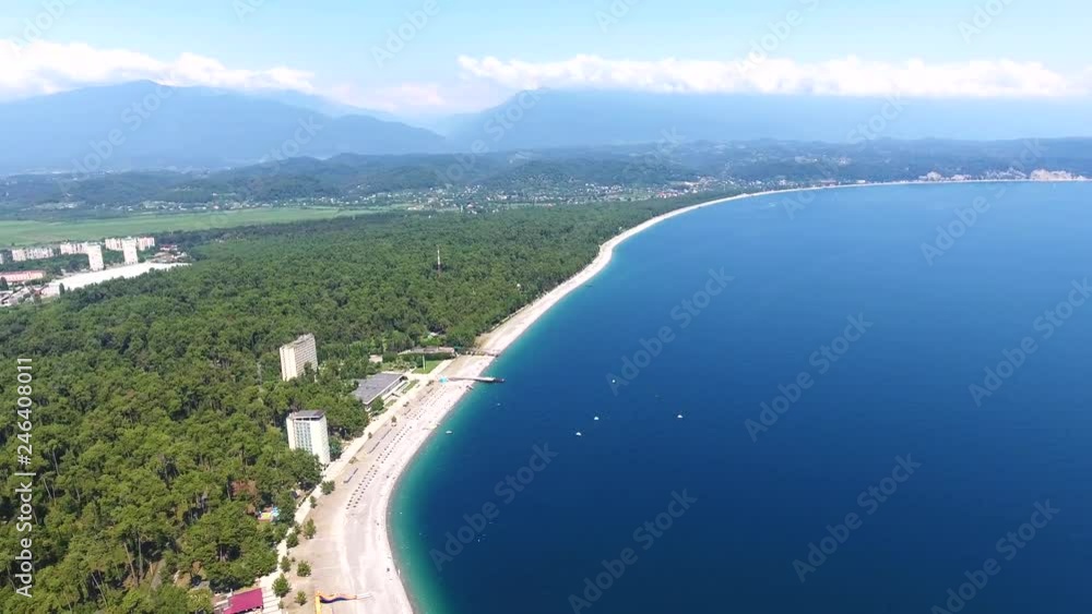 Aerial: coastline in blue bay is a beach hotel with umbrellas in amazing sand beach, green pines forest, relax resort Pitsunda on Abkhazia. Aerial: coastline in blue bay is a beach hotel with umbrellas in amazing sand beach, green pines forest, relax resort Pitsunda on Abkhazia.