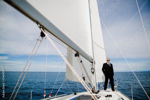 Mann mit Anzug steht auf einem Boot unter Segeln