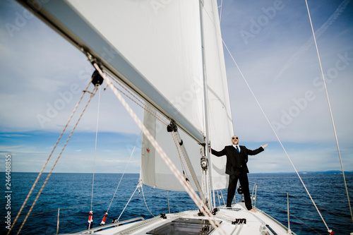 Mann mit Anzug jubelt auf einem Boot unter Segeln