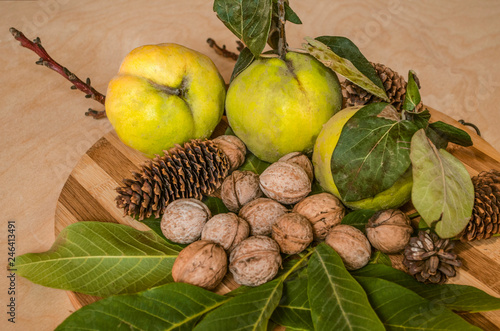 Striped wooden kitchen board with autumn fruits, quince with withered leaves, a handful of walnuts in a shell and pine cones


