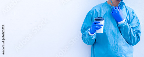 Doctor in blue scrubs relaxing with coffee break.Doctor or medic holding coffee to go cup isolated on white background.