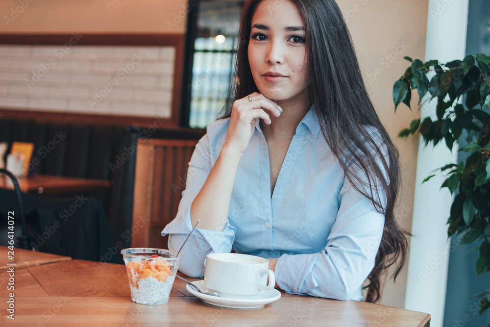 Beautiful charming brunette smiling Asian girl has Breakfast with coffee and Chia pudding at cafe Beautiful charming brunette smiling Asian girl has Breakfast with coffee and Chia pudding at cafe