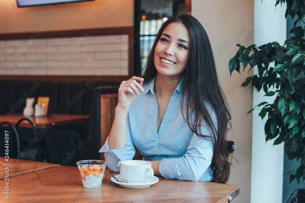 Beautiful charming brunette smiling Asian girl has Breakfast with coffee and Chia pudding at cafe