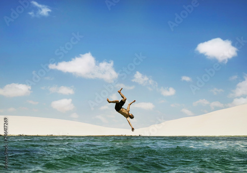 Man jumping backflip on lake with dunes in background, Lençois Maranhenses, Brazil