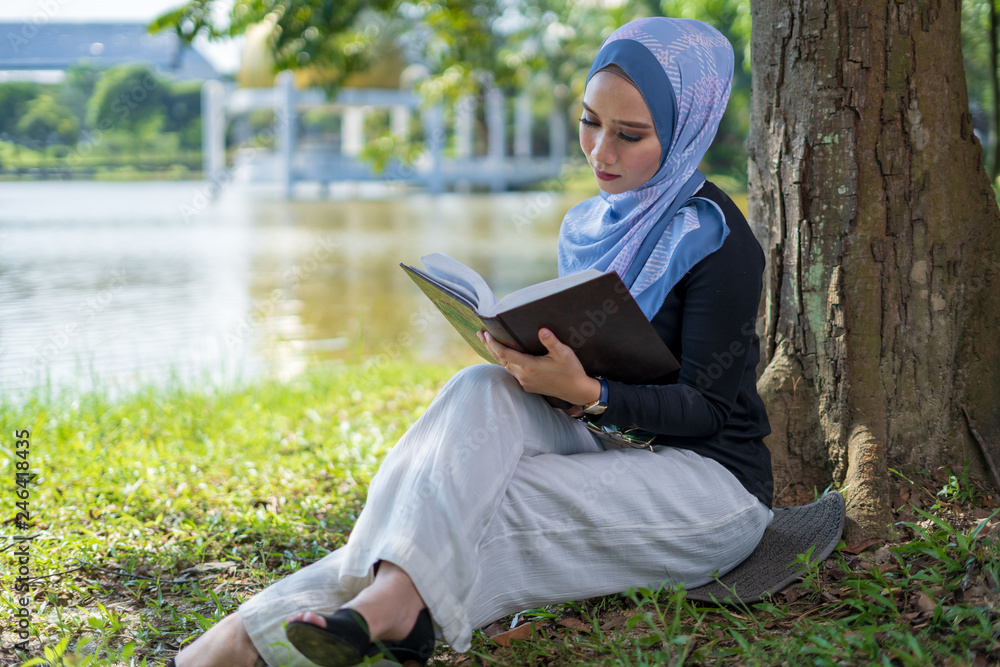 Attractive young woman reading book under the tree. Education concept.