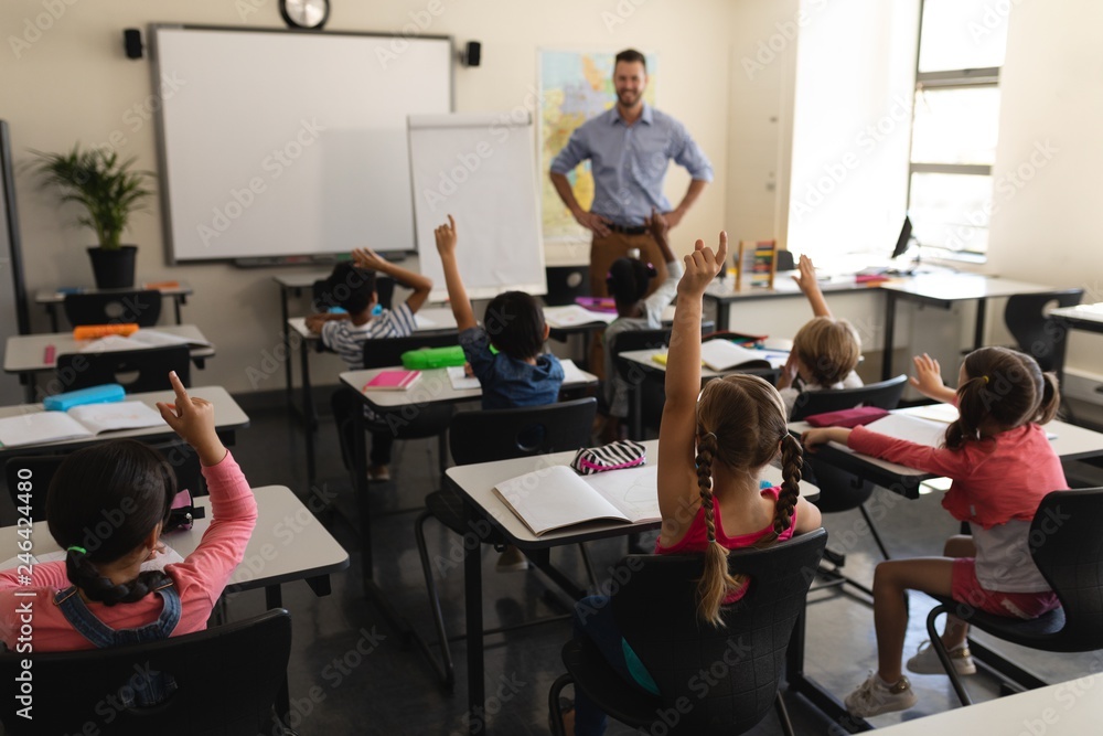 Fototapeta premium School kids raising hand in classroom