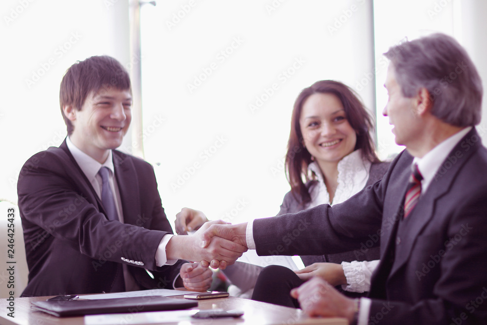 handshake of business partners sitting at a Desk handshake of business partners sitting at a Desk