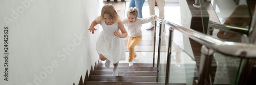 Happy kids go upstairs to second floor their new modern house, family moving day relocation and loan, buy first home concept. Horizontal photo banner for website header design with copy space for text
