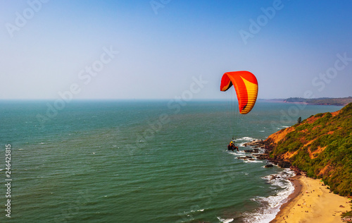 Paragliding in the sky. Paraglider tandem flying over the sea with blue water and mountains in bright sunny day. Aerial view of paraglider and Blue Lagoon in goa India at . Extreme sport. Landscape