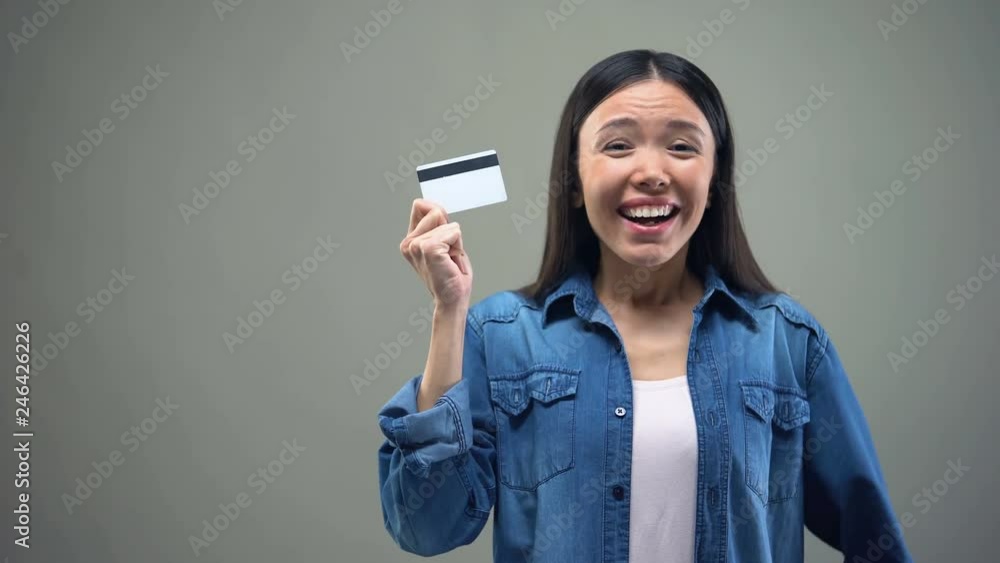 Asian woman holding credit card in hands, cash back services, grey background Asian woman holding credit card in hands, cash back services, grey background