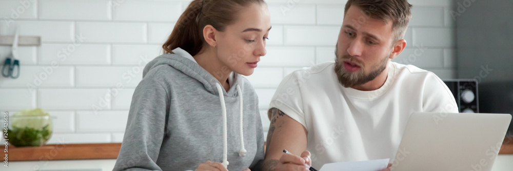 Fototapeta premium Horizontal photo millennial couple sitting at table check utilities bills read leasing loan documents. People planning family budget concept, banner for website header design with copy space for text
