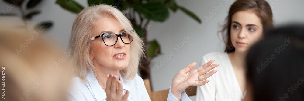 Aged businesswoman coach teach give instructions knowledge to new employees generation people gather at seminar receive new information ideas concept. Horizontal photo banner for website header design - obrazy, fototapety, plakaty 