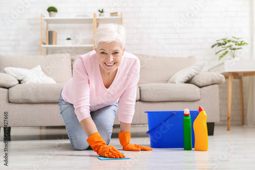 Smiling mature housewife cleaning floor at home